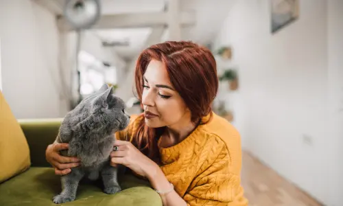 Red-haired woman gently kissing her gray cat, illustrating the bond that makes hiring pet sitters a necessity, as detailed in our Ultimate Guide to Pet Sitting: Ensuring Your Pets Are Happy While You're Away.