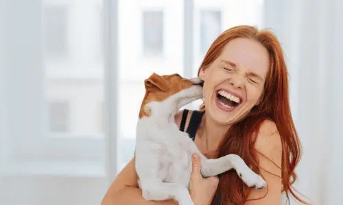 Joyful woman laughing as she hugs her dog, perfect for understanding the importance of hiring pet sitters from our Ultimate Guide to Pet Sitting: Ensuring Your Pets Are Happy While You're Away.